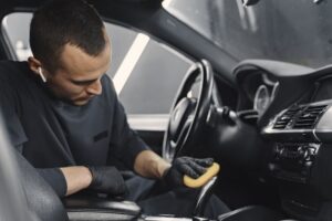 Detailer wearing black gloves cleans the center console and armrest area inside a vehicle.
