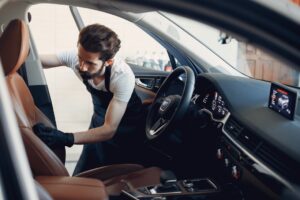 Detailer cleaning the brown leather front seat inside a vehicle during an interior detailing service.