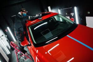 Technician polishing the roof of a red car with a machine buffer inside a detailing bay.