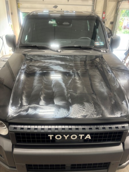 Black Toyota SUV hood with ceramic coating product spread across the paint during detailing service.