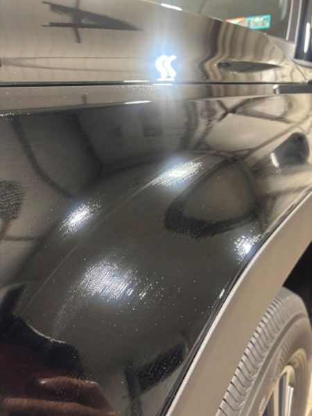 Close-up of a black vehicle side panel showing a glossy ceramic coated finish with light reflections.