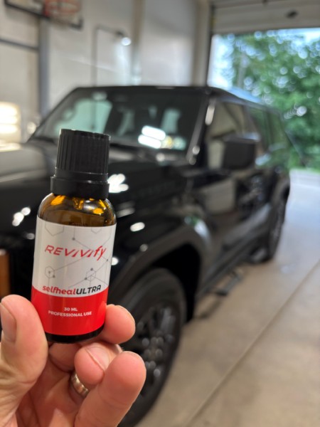 Hand holding a bottle of Revivify Self-Heal Ultra ceramic coating in front of a black Toyota SUV.